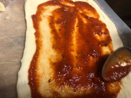 spreading spaghetti sauce on dough