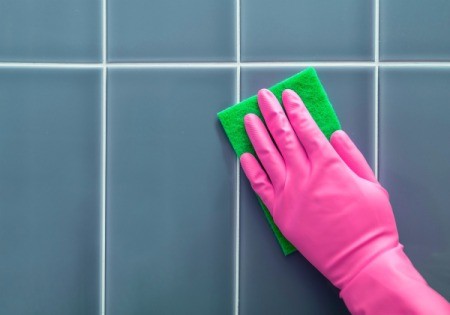 Hand in pink rubber glove scrubbing tile wall.