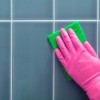 Hand in pink rubber glove scrubbing tile wall.