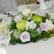 Candle centerpiece with apples roses and sprigs of fir.