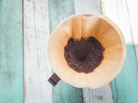 Coffee filter with coffee grounds on a painted wood backdrop.