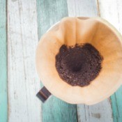 Coffee filter with coffee grounds on a painted wood backdrop.