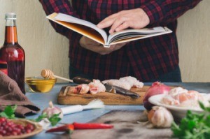 Man reading recipe book while prepping chicken surrounded by ingredients