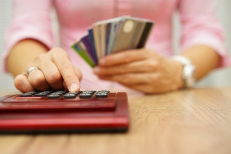 Woman holding a stack of credit cards and typing into a calculator.