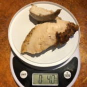 A plastic lid on top of a food scale, weighing chicken breasts.