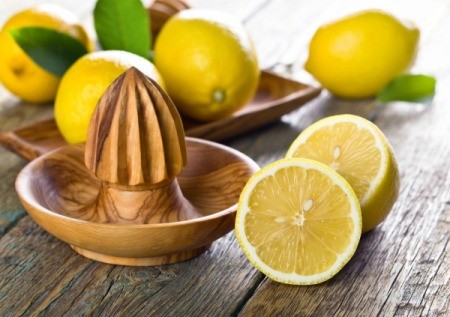 Wooden lemon juicer surrounded by lemons.
