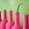 Line of wine bottles painted bright pink with a green blade of grass sticking out of one.