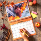 Open wall calendar with rustic October image, female hand ready to write in square with pencil.