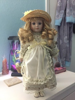 Identifying a Porcelain Doll - doll wearing a straw hat and a print dress with a lace edged apron