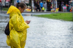 Girl in a rain poncho during a flood, using a phone.