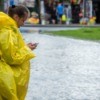 Girl in a rain poncho during a flood, using a phone.