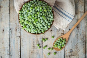 Frozen peans in a bowl with a wooden spoon on a weathered wood background.