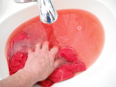 A red t-shirt that is being washed in the sink to remove the excess dye.