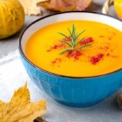 Bowl of squash soup with a sprig of rosemary and chili powder.
