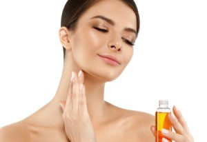 Woman putting oil on her face while holding a small bottle of oil.