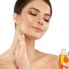 Woman putting oil on her face while holding a small bottle of oil.