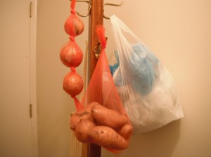 A coat rack with hanging onions, potatoes and extra plastic bags.