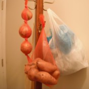 A coat rack with hanging onions, potatoes and extra plastic bags.
