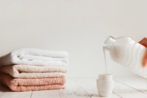 Hand pouring laundry soap into cap next to a pile of folded towels.