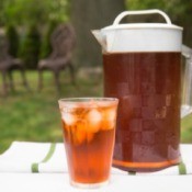 Pitcher and glass filled with ice tea on an outdoor table.