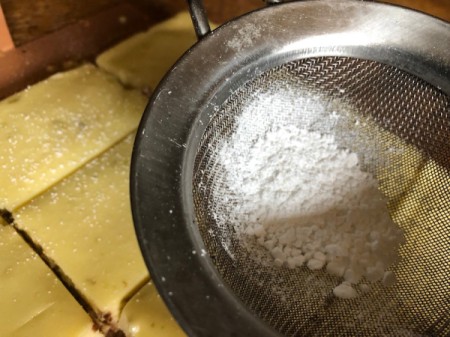 dusting Cheesecake Bars with powdered sugar