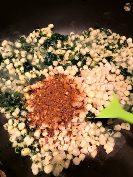 adding spices to corn and spinach
