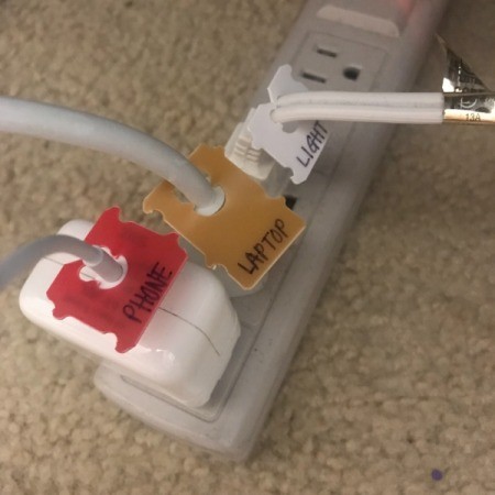 Bread tags marked with the names of electronic equipment, placed on cords in a power strip.