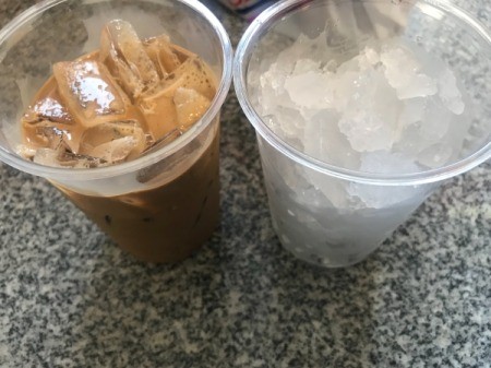 Vietnamese coffee poured into one cup with ice, with another cup with ice remains empty.