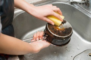 Washing a burnt pot in a sink.