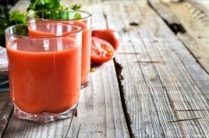 Two glasses of tomato juice on a rustic wood table.