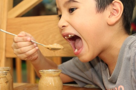 A boy eating butterscotch pudding from a jar.