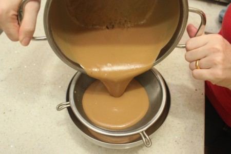 Cooked butterscotch putting being strained into a bowl.