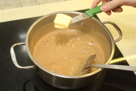 Butterscotch pudding being cooked on the stove, with butter being added.