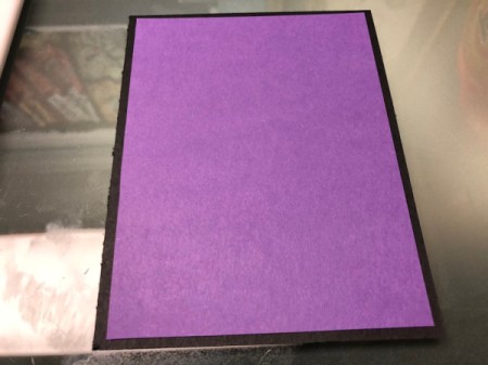 A piece of purple paper adhered to the front of a black folded card.