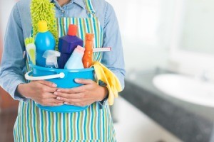 Person in an apron holding a bucket of cleaning supplies.