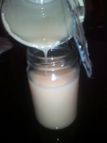 An open can of condensed milk being stored in a glass jar.