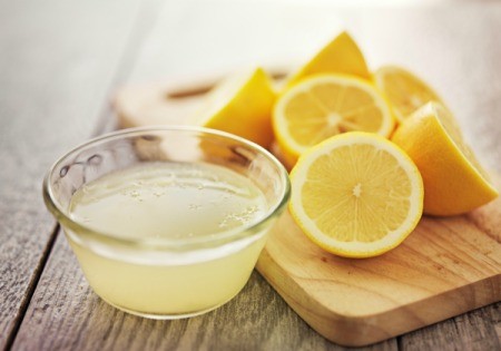 Bowl of lemon juice next to cut lemons.