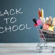 "Back to School" written on a chalk board with a small shopping cart full of school supplies.