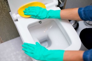 Someone cleaning a toilet seat with a large sponge.