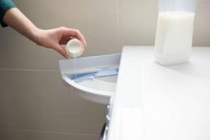 Hand pouring liquid fabric softener into washing machined soap dispenser.