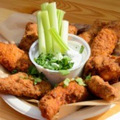 Fried chicken around a cup of ranch dressing with celery sticks.