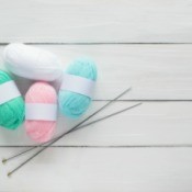 Pink, white, green and blue skeins of yarn with a pair of knitting needles.