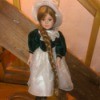 Value of a Porcelain Doll - doll wearing a green velvet bodice dress with a white lace skirt and matching hat