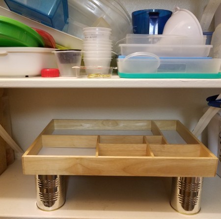 A shadowbox frame set on four cans in a pantry.