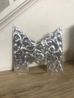 Foil Wrapped Cardboard Letter - letter standing on the floor next to the stairs