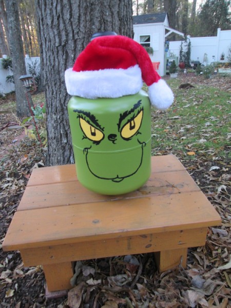 Helium Tank Upcycled as The Grinch - Grinch on a wood stool in the garden
