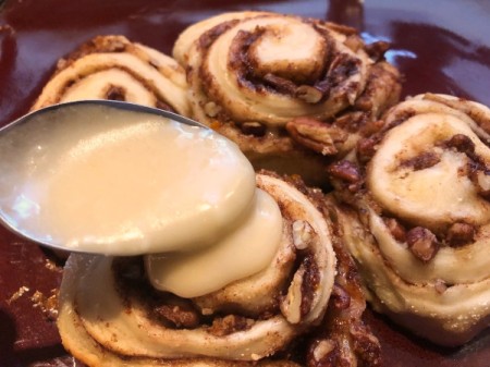 spooning frosting on Cinnamon Rolls