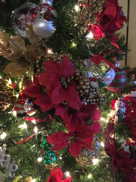 An artificial Christmas tree decorated with poinsettias, gold berries and white lights.