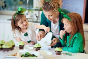 2 girls and a woman wearing green, decorating green cupcakes.