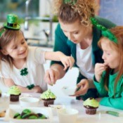 2 girls and a woman wearing green, decorating green cupcakes.